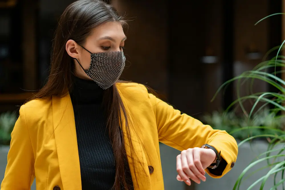 Woman in yellow blazer looking at smartwatch outdoors